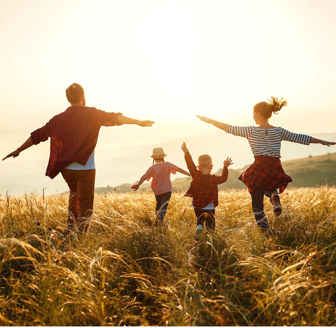 A family running through a golden field at sunset, arms wide
