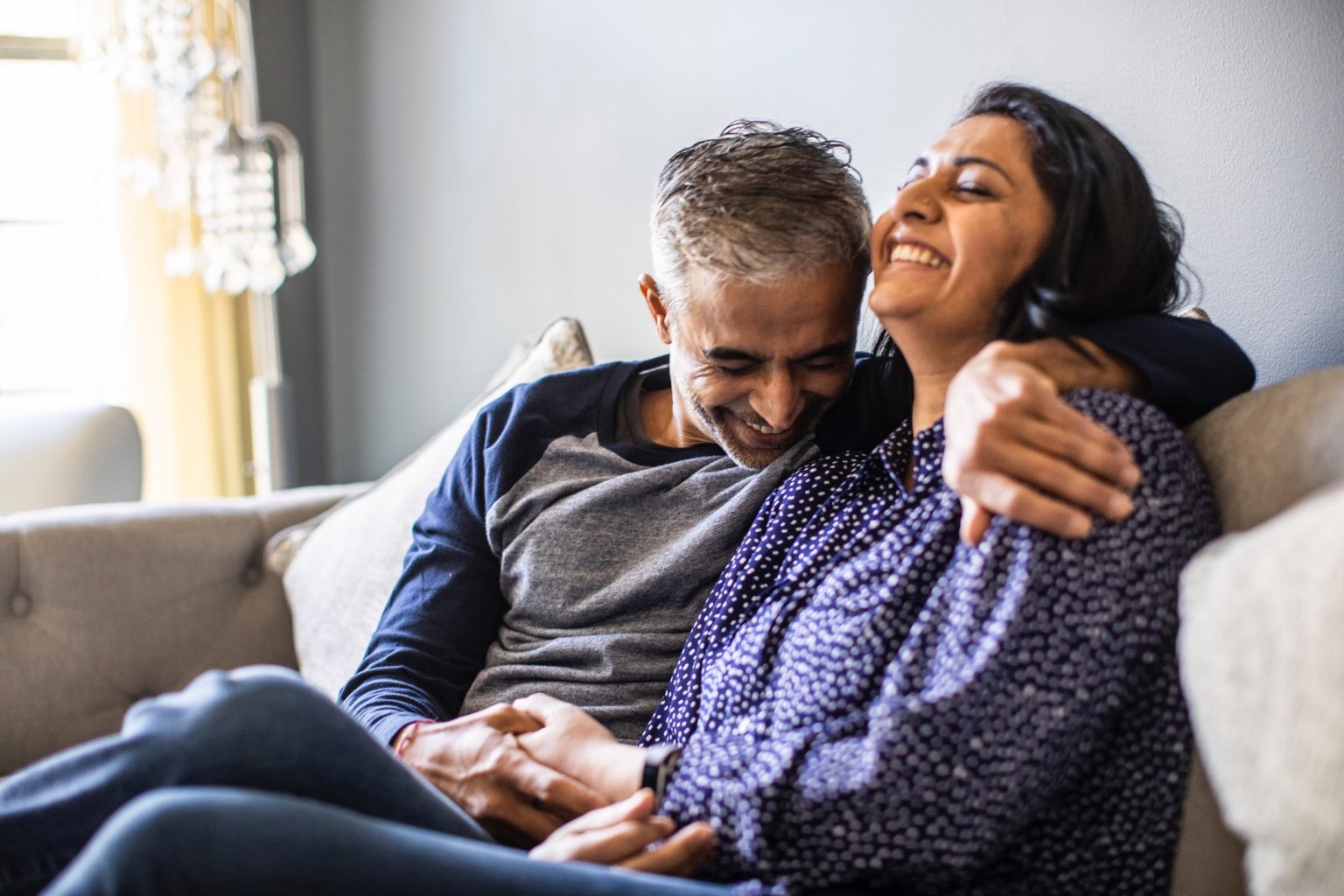 An older couple laughing together on a sofa, her head on his shoulder