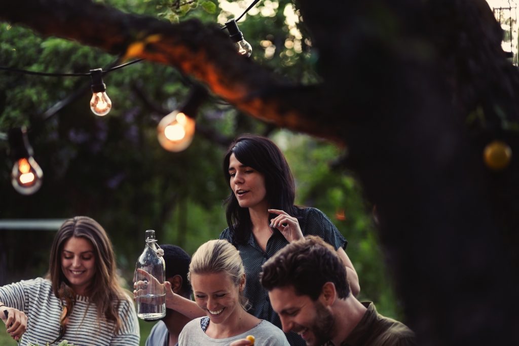 Friends laughing together at an outdoor table under string lights