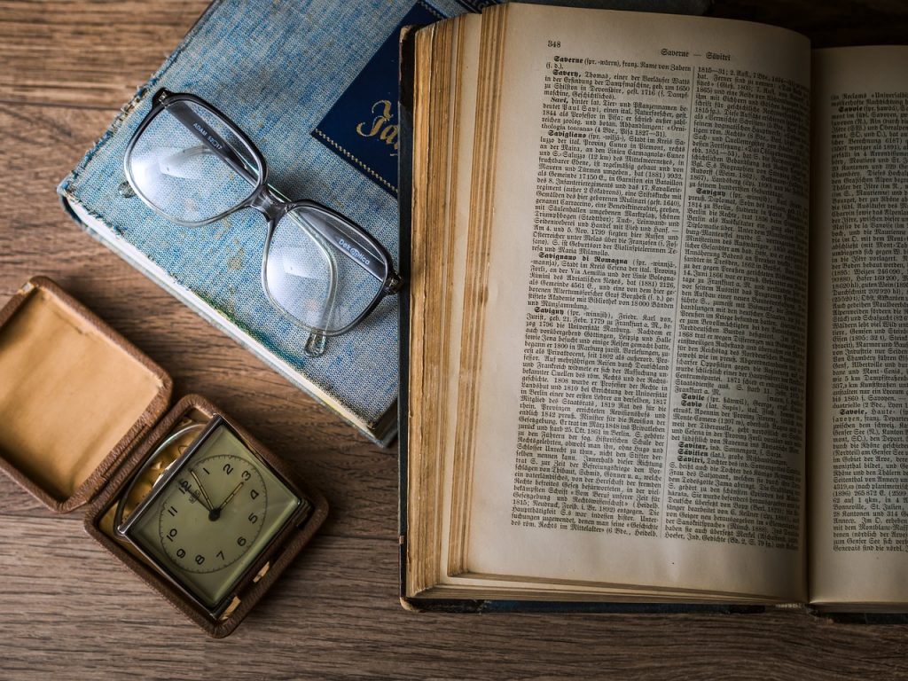 An open book, reading glasses, and a pocket watch on a wooden table