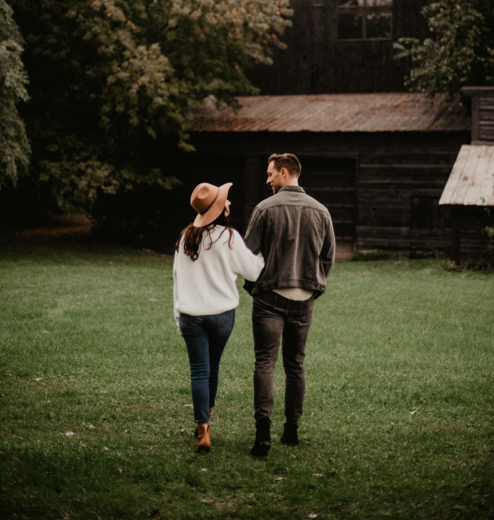 A couple walks through a grassy area towards a rustic barn, capturing a romantic autumn ambiance.