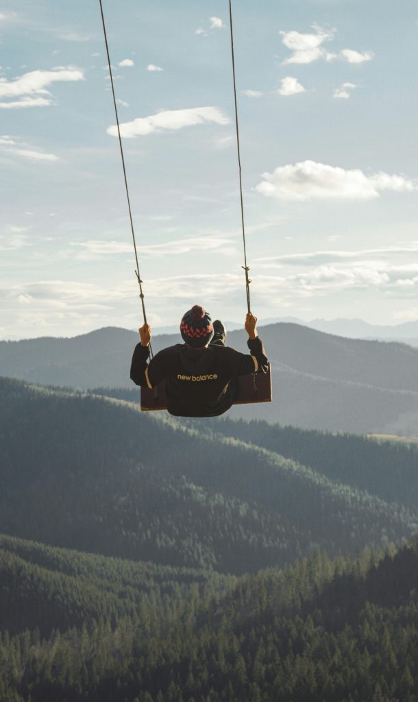 Boy in helmet swinging high above serene mountain landscape, enjoying leisure and nature's beauty.