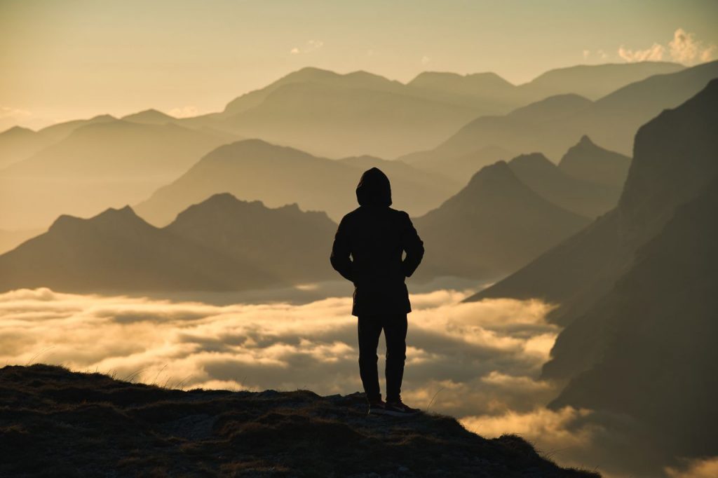 Silhouette of person overlooking misty mountains with dramatic sunrise lighting.