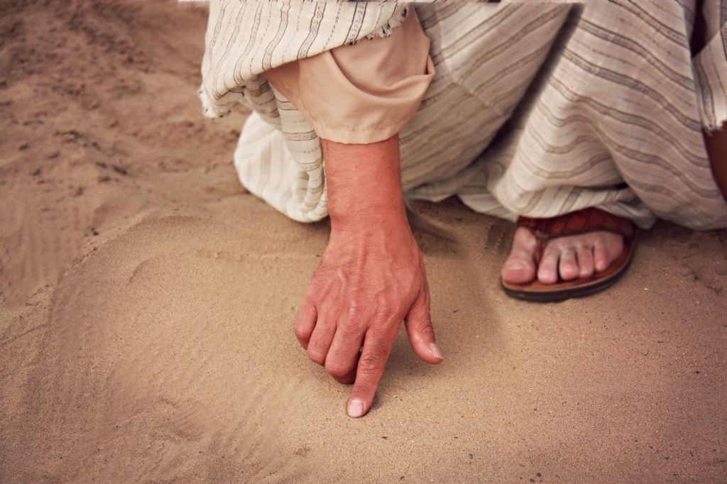 Close-up of a person drawing in sand with a finger outdoors, wearing traditional attire.
