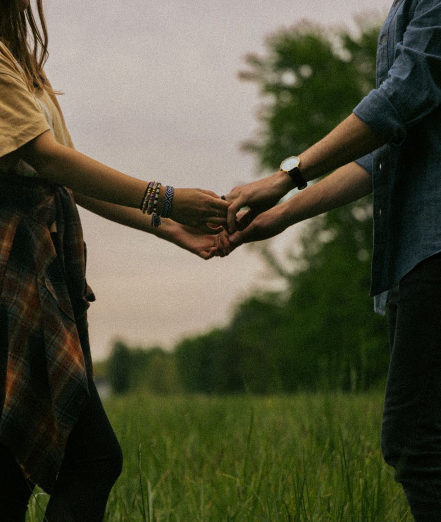 A couple holding hands in a lush green meadow, showcasing love and togetherness in a summer setting.